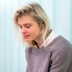 Alina Tomnikov istuu kuvassa silmät kiinni, taustalla valoa ja lasiseinä.