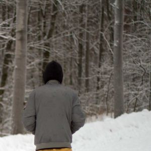 30-åriga Ali på en snöig skogsväg i Finland. Han står med ryggen vänd mot kameran och en huva på huvudet.