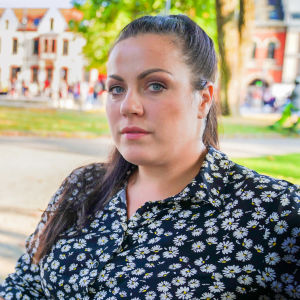 Kaisa Augusta Hansén-Suckow sitter på en parkbänk i solen och tittar in i kameran.