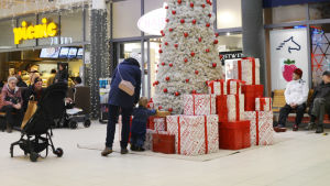 Julen brukar vara en viktig tid för små barn. Julklapparna intresserar, även om de bara är dekorationer. En stor vit julgran står mitt i Lundi köpcentrum. En mamma och ett litet barn har stannat för att titta på de stora julpaketen som ligger som prydnader invid granen.