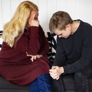 Äiti ja poika istuvat sohvalla, poika on surullinen ja äiti pitää kättä pojan olalla