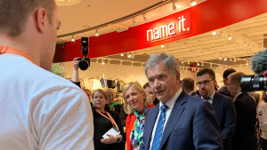 Till vänster syns en ung man som står bakom ett bord med läskedrycker på. Till höger synns president Sauli Niinistö..