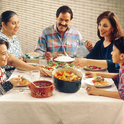 Familj som sitter runt ett bord och äter mat.