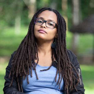 Rahel Weldeab Sebhatu tjänstgjorde i Eritreas militär år 2000. En kvinna sitter på en stol utomhus. Bakgrunden är grön. Hon ser bestämt in i kameran.