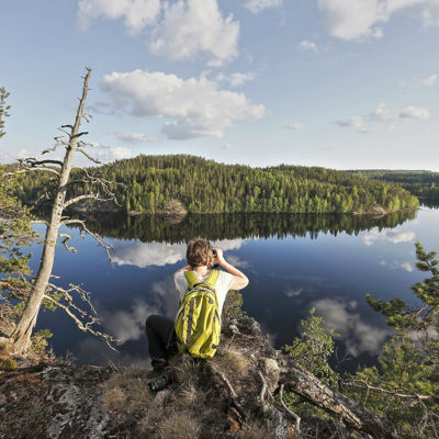 En man sitter på ett berg och tittar mot ett spegelblankt vatten