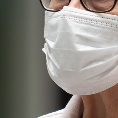Närbild på en person (kvinna) som använder ett vitt munskydd som täcker både mun och näsa.
