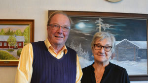 Rolf Björkell med frun Viola som också deltagit i föreningsarbetet. En äldre man och en äldre kvinna står framför en vägg prydd med oljemålningar.