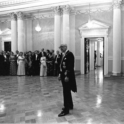 Tasavallan presidentin itsenäisyyspäivän vastaanotto Presidentinlinnassa 1975. Presidentti Urho Kekkonen seisoo yksin keskellä salia, taustalla vieraita ja valokuvaajia.