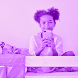 Lapsi istuu sängyssään puhelin kädessä.