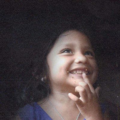 Hondurasilainen pikkutyttö hymyilee, kuvan tausta on tumma.