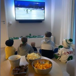 Spännande tider för Penttinens och grannen Strömbergs barn. Flera barn sitter på golvet framför en tv. Bakom dem på ett bord finns skålar med chips och choklad.