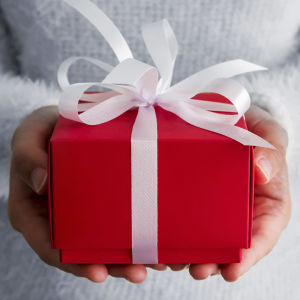 Punainen lahjapaketti, jossa valkoinen nauha, on naisen käsissä.