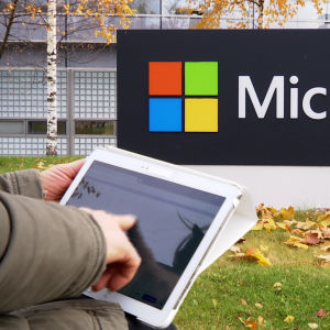 Microsoftin logo, jonka edessä tablettia pitelevä käsi.