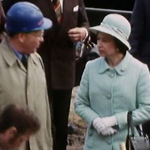 Kuningatar Elisabet seisoo ihmisten ympäröimänä, katsoo kypäräpäistä miestä. Vierailu Suomessa.