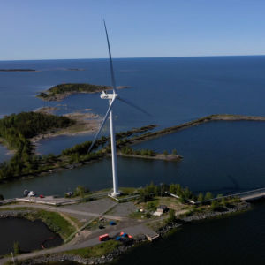 Ett vindkraftverk på en liten udde. Bakom möllan sträcker sig havet mot horisonten.