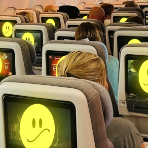 Ihmiset istuvat lentokoneessa ja katsovat näytöiltä hymynaamoja