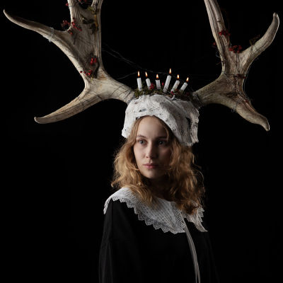 En ung kvinna bär på en krona av elghorn och levande ljus. 