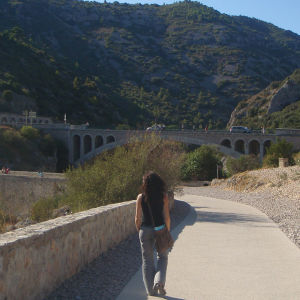 Nainen kävelee Hérault'n laaksoa reunustavalla kävelytiellä, taustalla vanhoja kaarisiltoja.