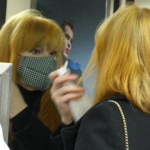 En kvinna med ansiktsmask speglar sig och rättar till håret. 