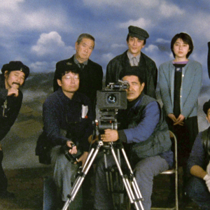 Kuvausryhmä poseeraa kameran takana, taustalla pilviä, kuva elokuvasta Elämän jälkeen, kuvassa myös teksti "Teeman elokuvafestivaali".