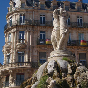 Veistos 'Kolme sulotarta' Montpellier'n keskusaukiolla, Place de la Comédiella, taustalla 1800-luvun kerrostalo.