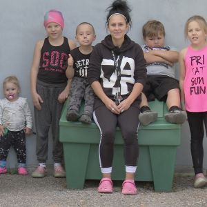 Äiti istuu viiden lapsensa kanssa roskalaatikon kannella