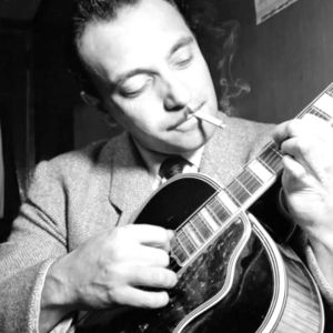 Django Reinhardt näppäilee kitaraa tupakka suussa, mustavalkoisessa kuvassa
