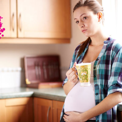 en gravid kvinna som står i sitt kök och dricker ur sin mugg