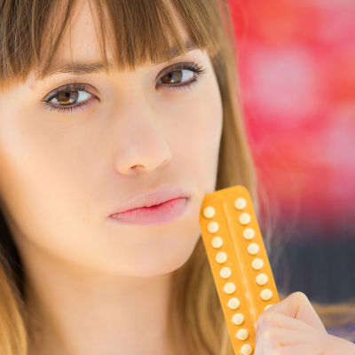 en ung kvinna som står med ett p-piller paket mot sin kind och ser seriös ut