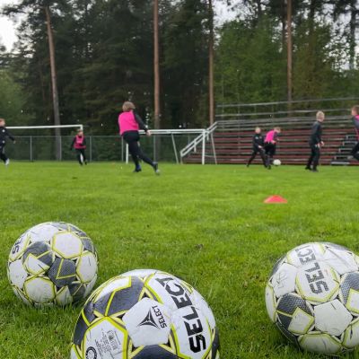 Kuvassa etualalla kolme jalkapalloa ja taaempana jalkapallojunioreita harjoituksissa