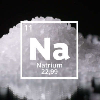 Natriums kemiska förkortning Na. I bakgrunden en hög med salt.