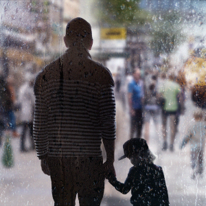 Mies seisoo lapsen kanssa käsikädessä vilkkaalla kadulla. Kuva otettu vesisateisen ikkunan läpi.