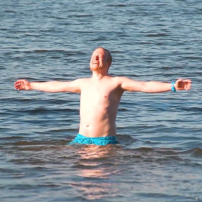 En glad man står i vattnet med badbyxor på sig.