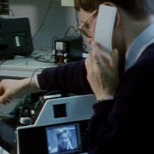 Mies puhuu kuvapuhelimessa naisen kanssa. Kuva on vuodelta 1990.