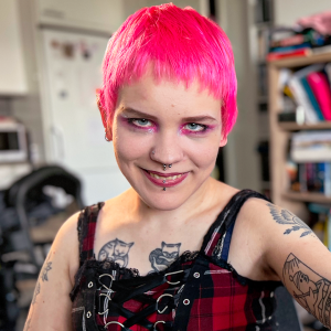 Nainen katsoo hymyillen kameraan kädessään piiska.