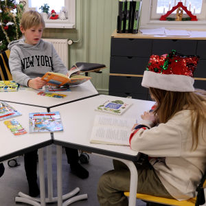 Tre barn sitter runt ett bord och läser böcker.