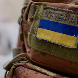 Nuhjuiseen armeijareppuun kiinnitetty ukrainan lippu tai Ukrainan armeijan tunnus. Sumeasta taustasta saattaa erottaa istuvan henkilön.