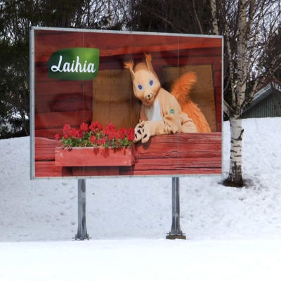 Talvisella tienvarrella Laihian kunnan tienvarsikyltti, jossa oravamaskotti ja Laihian kunnan logo