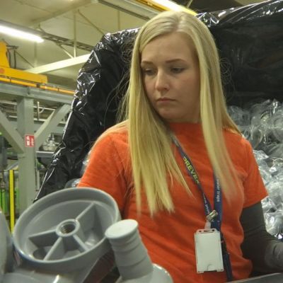 En kvinna står vid en fabrik och monterar plasdelar