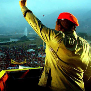 Presidentti Hugo Chávez puhuu suurelle ihmisjoukolle. Chávez seisoo selkä kameraan päin punainen baretti päässä. Hän on puristanut toisen kätensä nyrkkiin ja kohottanut sen ilmaan.
