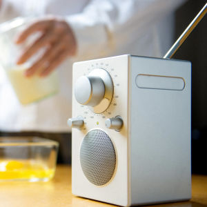 Keittiönpöydällä etualalla radiovastaanotin, jonka vieressä kananmunankuoria. Ihmishahmo mittaa taustalla sokeria, aikoo leipoa jotain.