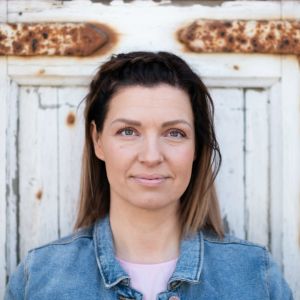 Monna Pursiainen seisoo vanhan, ruostuneen oven edessä.