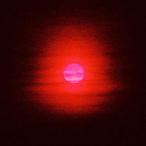 Teoskuvassa kirkkaan vaaleanpunainen taivaankappale, mahdollisesti kuu, loistaa punaisena mustaa taivasta vasten
