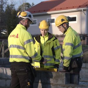 Byggstuderande har kunnat jobba utomhus mer eller mindre som normalt under corona-tiden. Tre unga män står tillsammans i gula kläder och hjälmar den ena håller en motorsåg