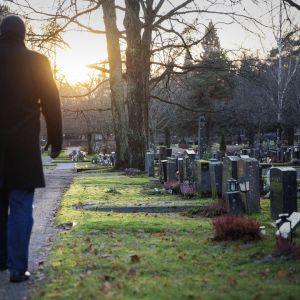 Mies kävelee kohti laskevaa aurinkoa hautausmaalla