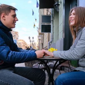 Nuori pariskunta istuu kahvilan terassilla ja pitää toisiaan kädestä.