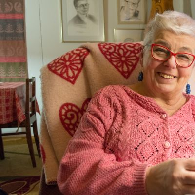 Nainen neuloo ja hymyilee.