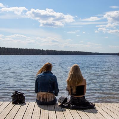 Kaksi nuorta naista istuu laiturilla järvellä keväällä.