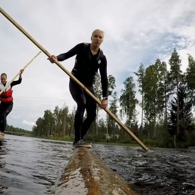 Iida Mäntylä ja Milla Sulkakoski tasapainoilevat tukkien päällä joessa.