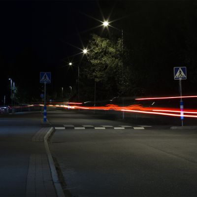 Pimeällä kadulla pitkällä valotusajalla otetussa valokuvassa auton valojen jättämät viirut.